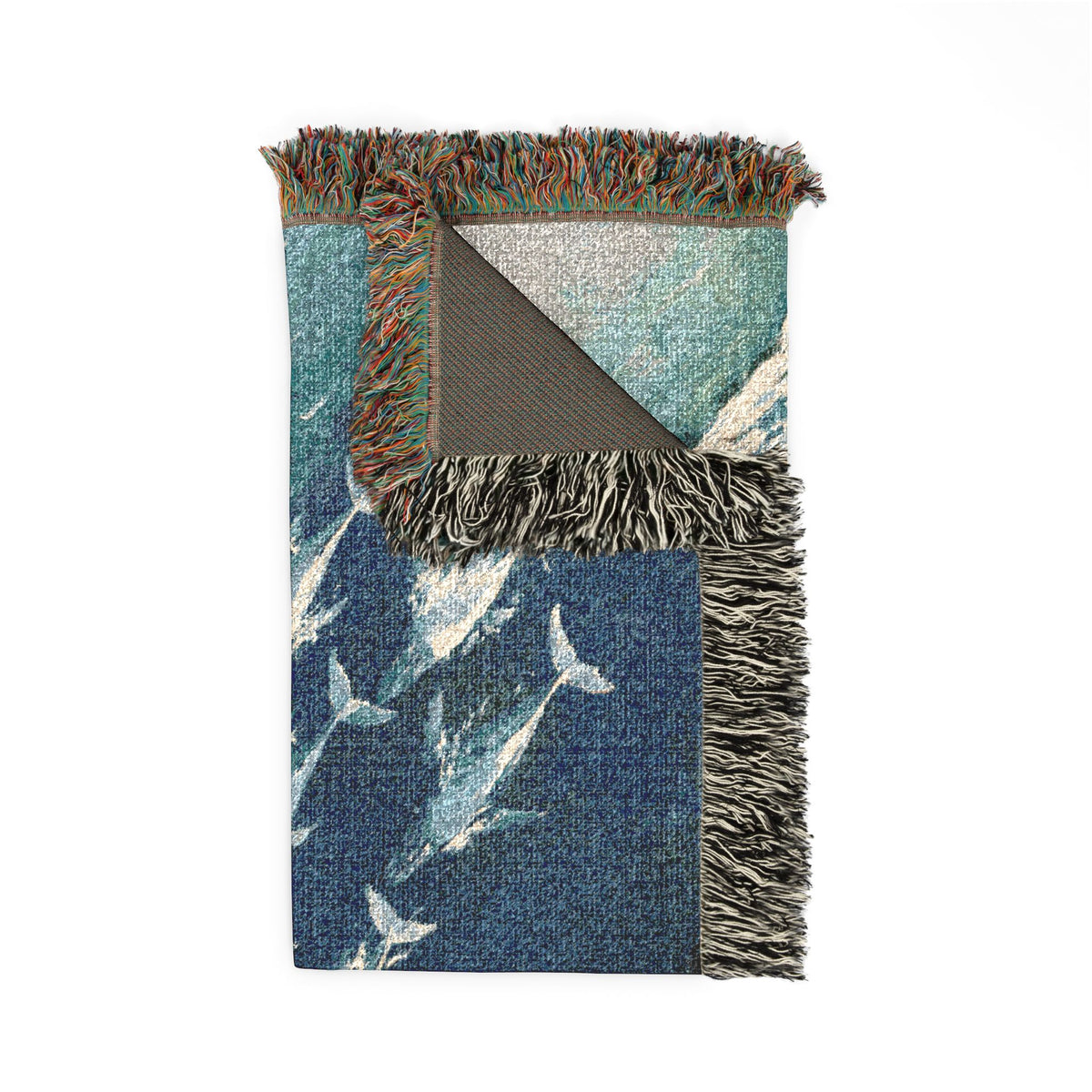 A folded woven throw blanket with fringe, featuring a blue and teal fish pattern on one side and a gray reverse side, shown on a white background.