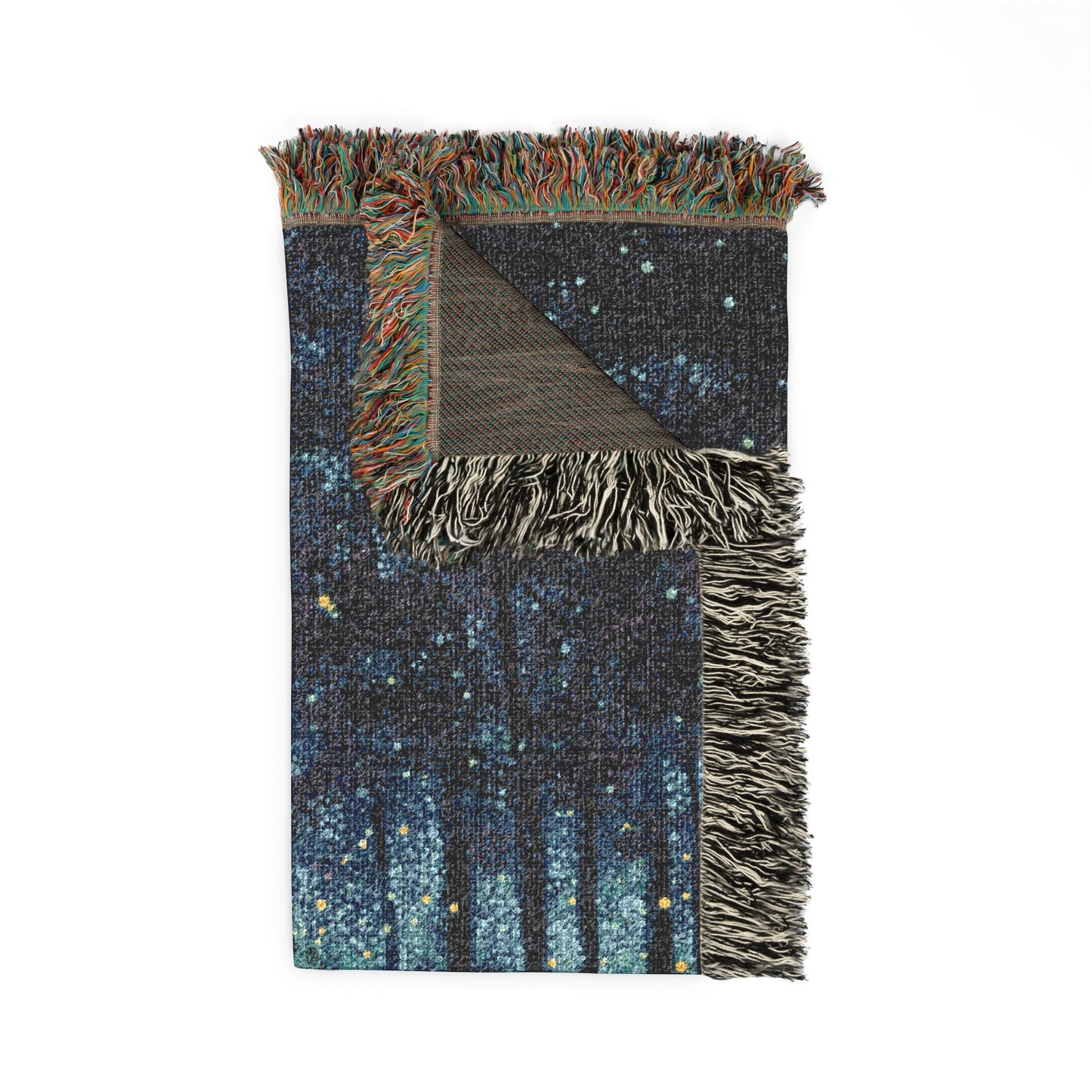 A folded woven throw blanket with multicolored fringe, featuring a dark blue and black starry night sky pattern with vertical tree silhouettes and small yellow and light blue stars, shown on a plain white background.