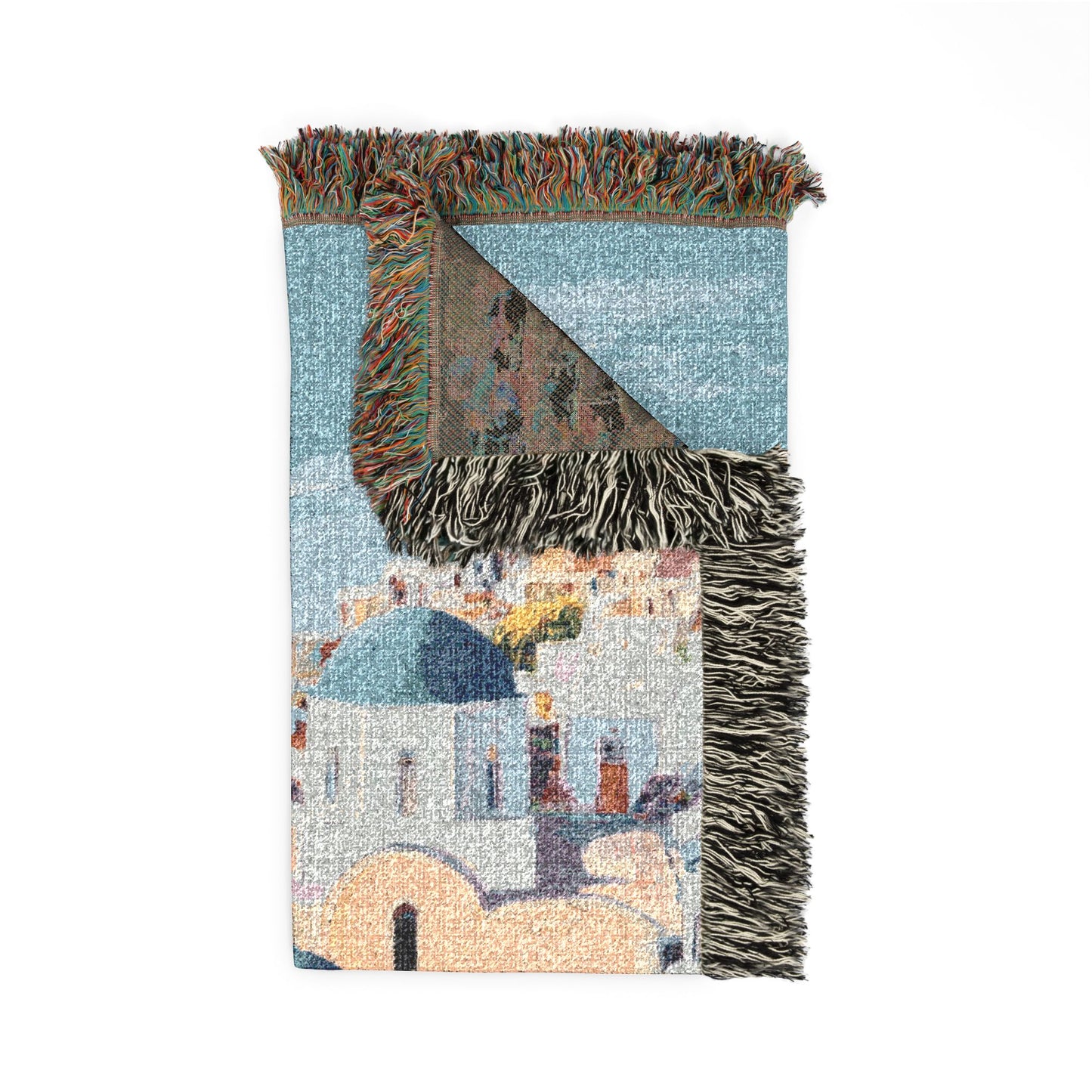 A rectangular woven throw blanket with multicolored fringe, featuring a scenic architectural print of white buildings with blue domes on a light blue background.