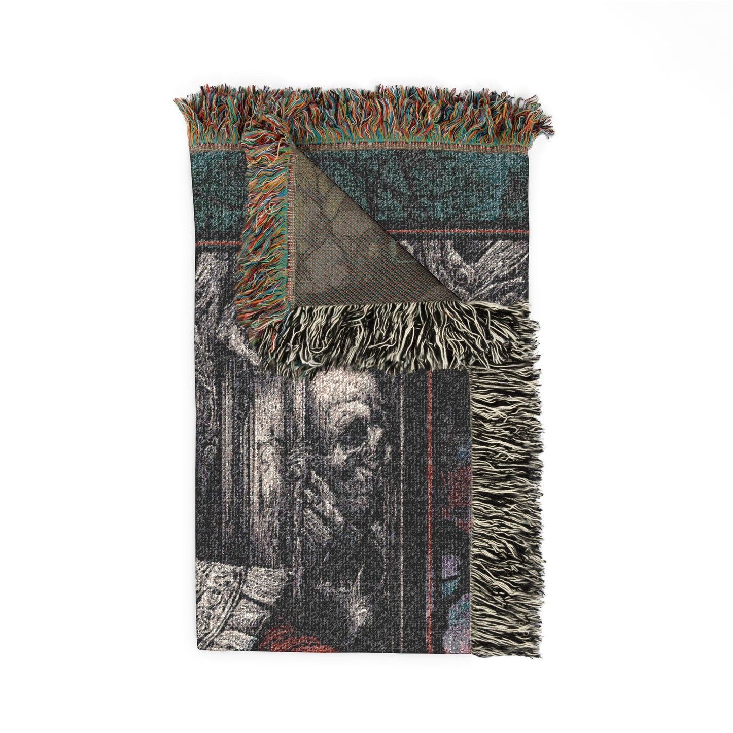 A folded woven throw blanket with multicolored fringe, featuring a dark, gothic-style graphic print of a skull in a doorway, shown on a solid white background.