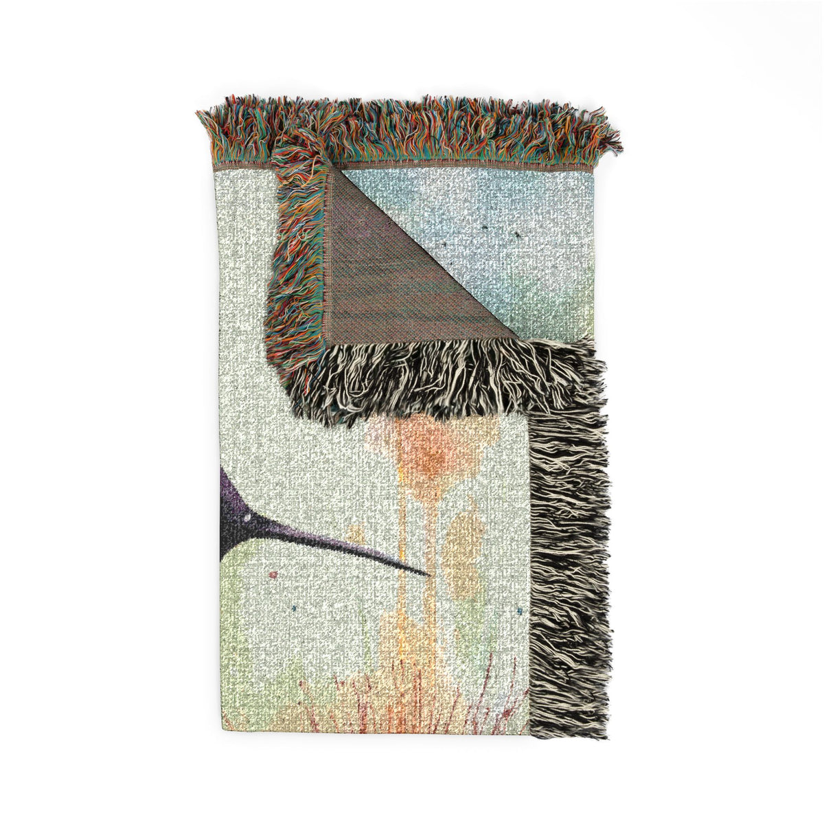 A rectangular woven throw blanket with multicolor fringe, featuring an abstract design with a triangular corner turned up to reveal the reverse side. The front displays a light gray and white textured background with a dark bird silhouette and orange paint-like drips, while the reverse side shows a blue-gray patterned section and a brown triangular panel.