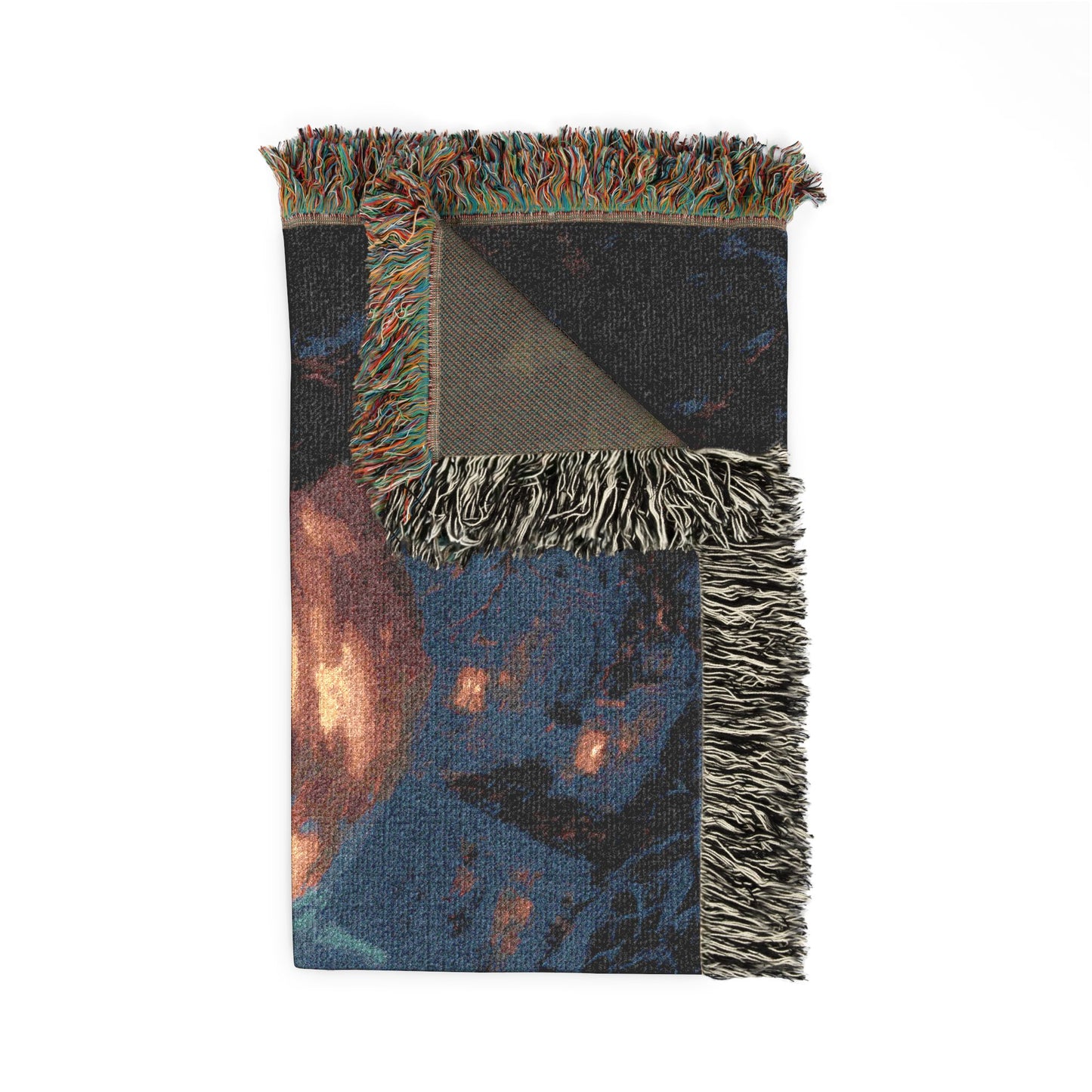 A folded woven throw blanket with multicolor fringe, featuring a dark blue and black abstract pattern with warm orange and brown highlights, and a solid taupe underside.