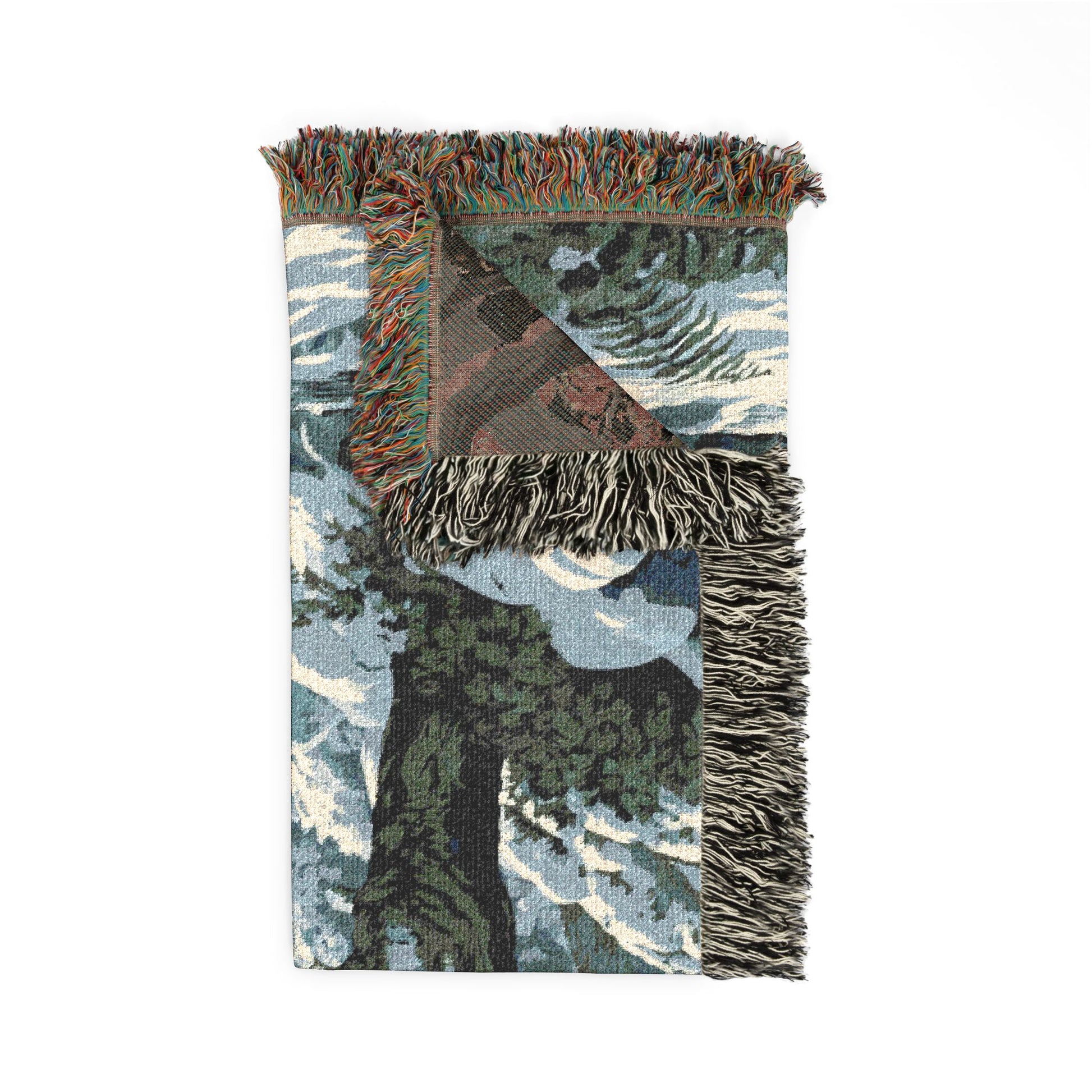 A woven throw blanket featuring a winter forest scene with snow-covered trees, fringed edges, and a folded corner revealing a brown patterned lining, shown on a plain white background.