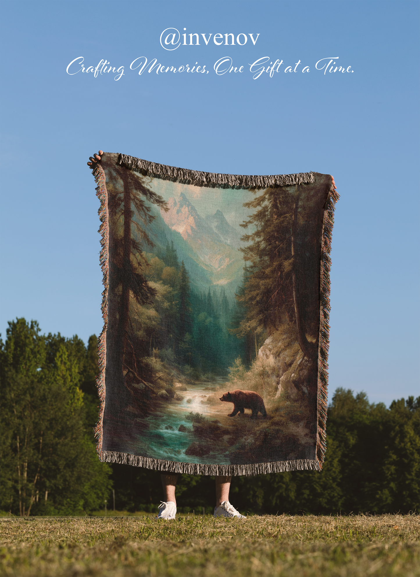 Person holding a woven blanket with a bear and forest design outdoors.