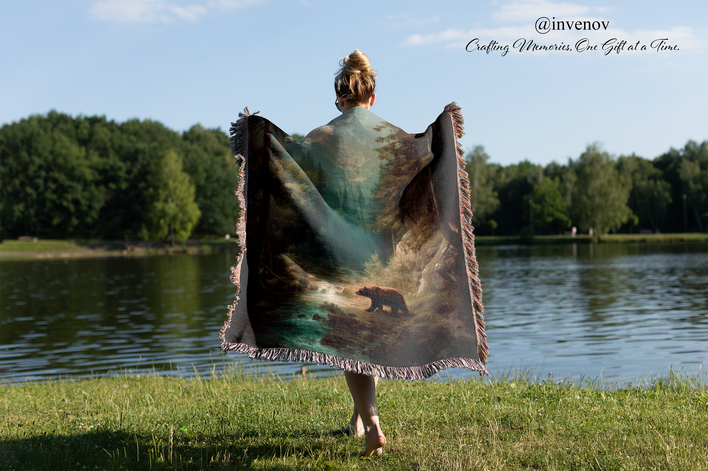 Person holding a bear-themed blanket by a lake with trees in the background