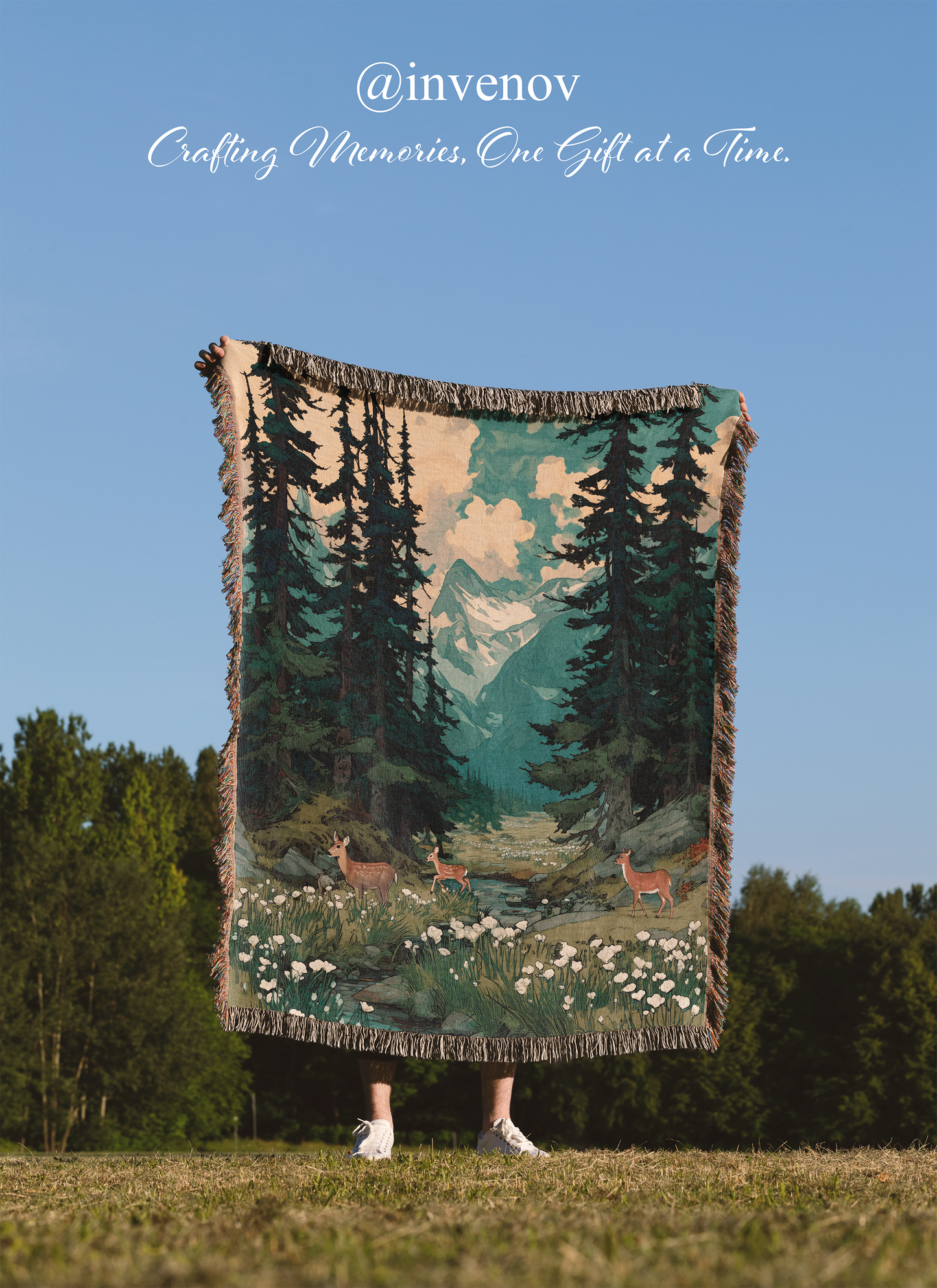 Person holding a forest-themed blanket with trees and deer in a field