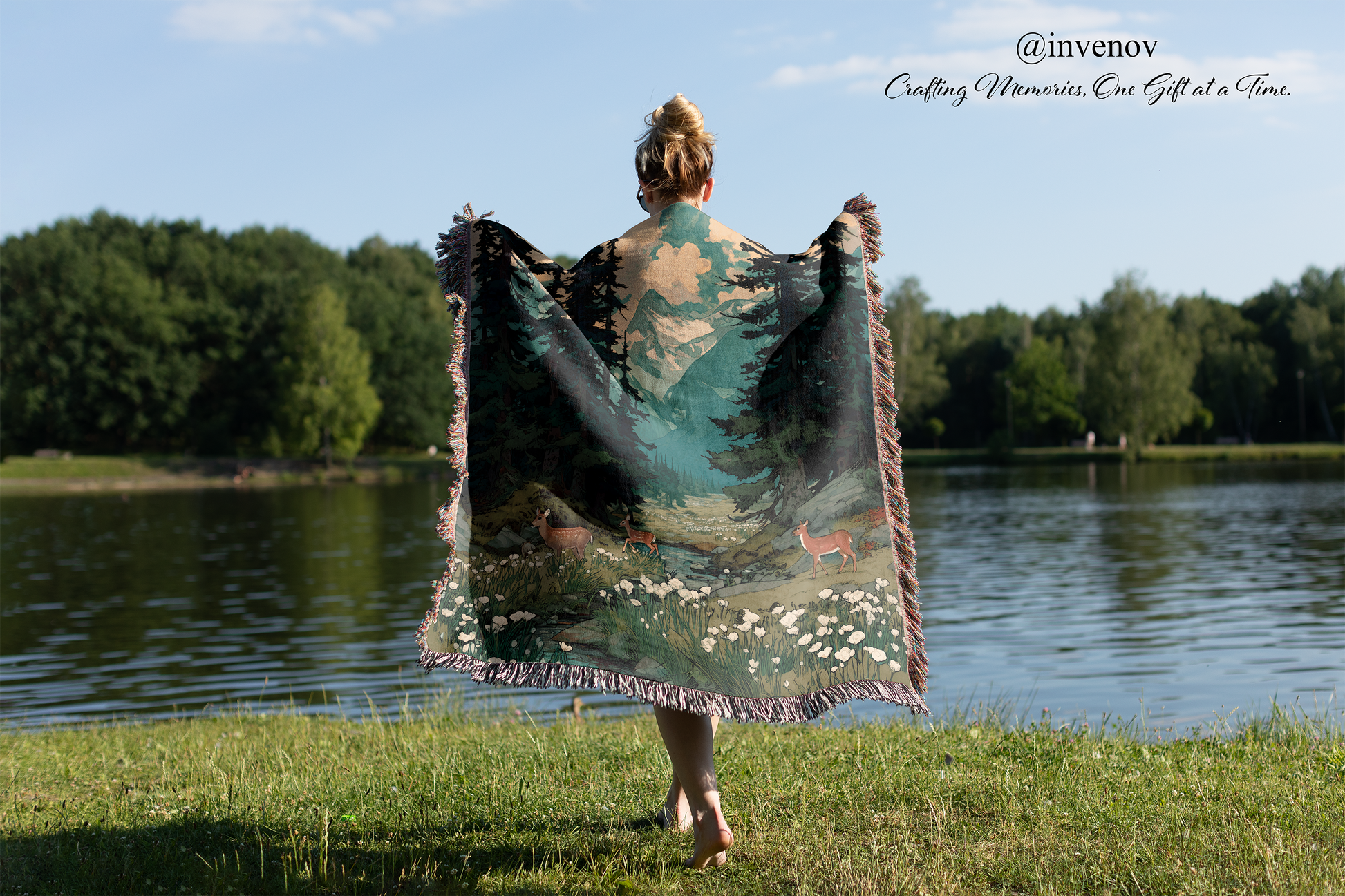 Person holding a large, decorative blanket by a lake with trees in the background