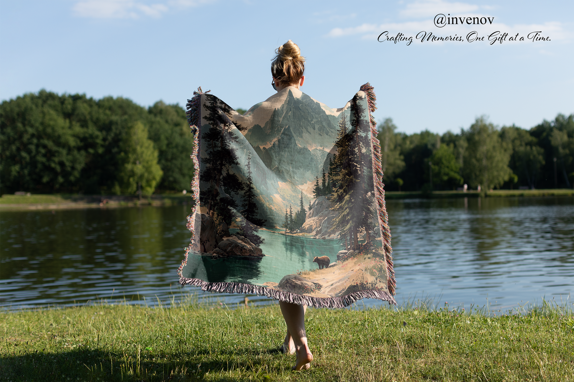 Person holding a scenic blanket by a lake with trees in the background