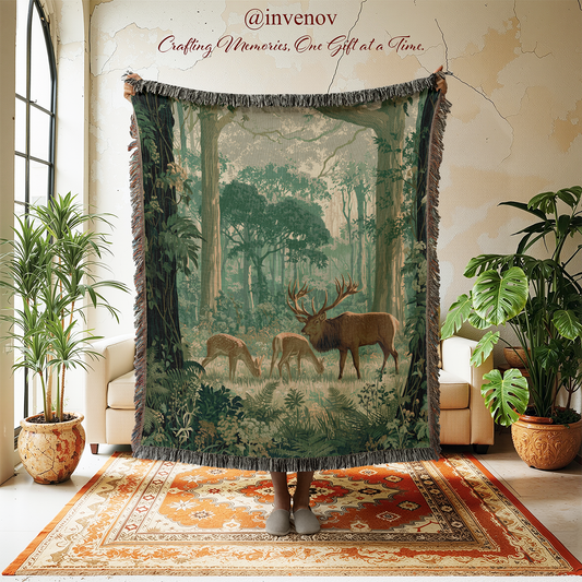 A large fringed throw blanket featuring a forest scene with deer is held up in a living room setting. The blanket depicts a lush green woodland with a stag and two fawns, and the background shows a person's feet at the bottom, flanked by potted plants and a patterned rug.