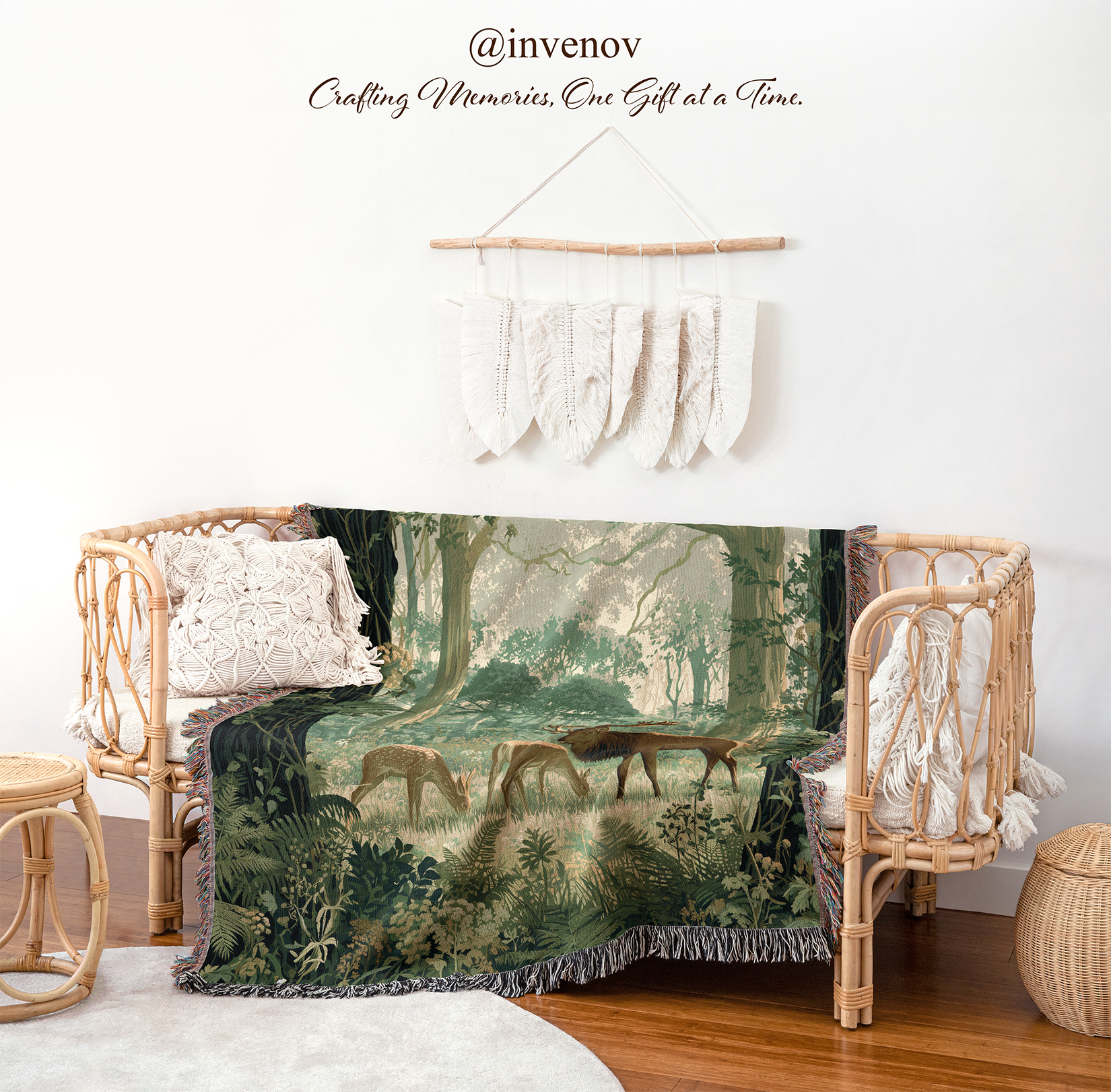 A woven throw blanket featuring a vintage forest scene with deer, draped over a rattan daybed in a styled room setting. The scene includes a rattan daybed, white textured pillows, a small woven stool, a wooden floor, and a white wall with a decorative macrame wall hanging.