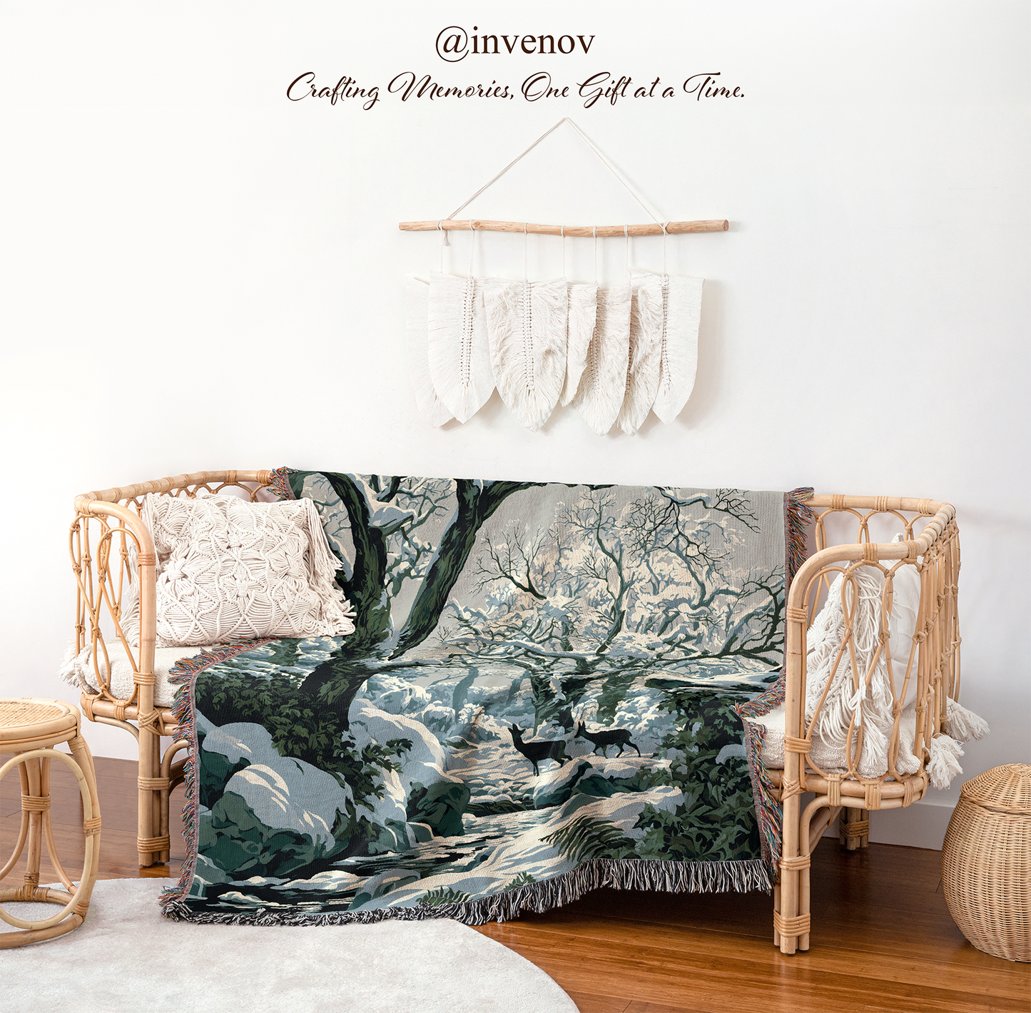 A winter forest landscape throw blanket with snow-covered trees is draped over a rattan bench in a styled room setting. The scene includes a white wall with decorative macrame hanging, a wooden floor, and a small woven basket.