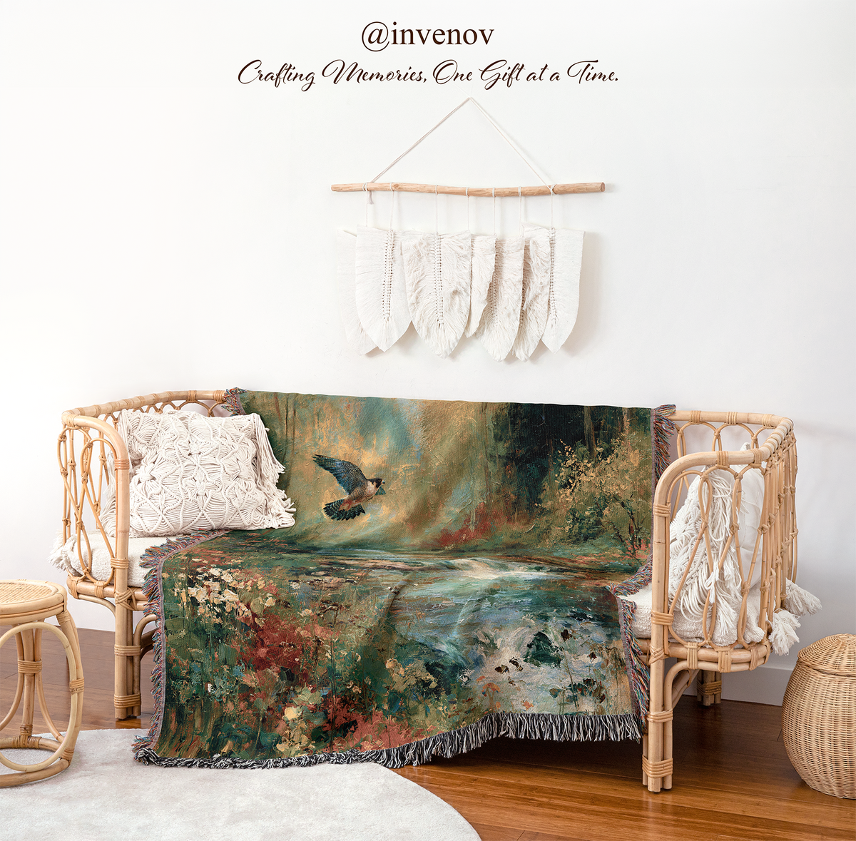 A woven rattan daybed styled in a bohemian room setting, draped with a large, colorful landscape throw blanket featuring a bird and watercolor-like scenery. The room has a white wall decorated with a macrame wall hanging, and a wooden floor.