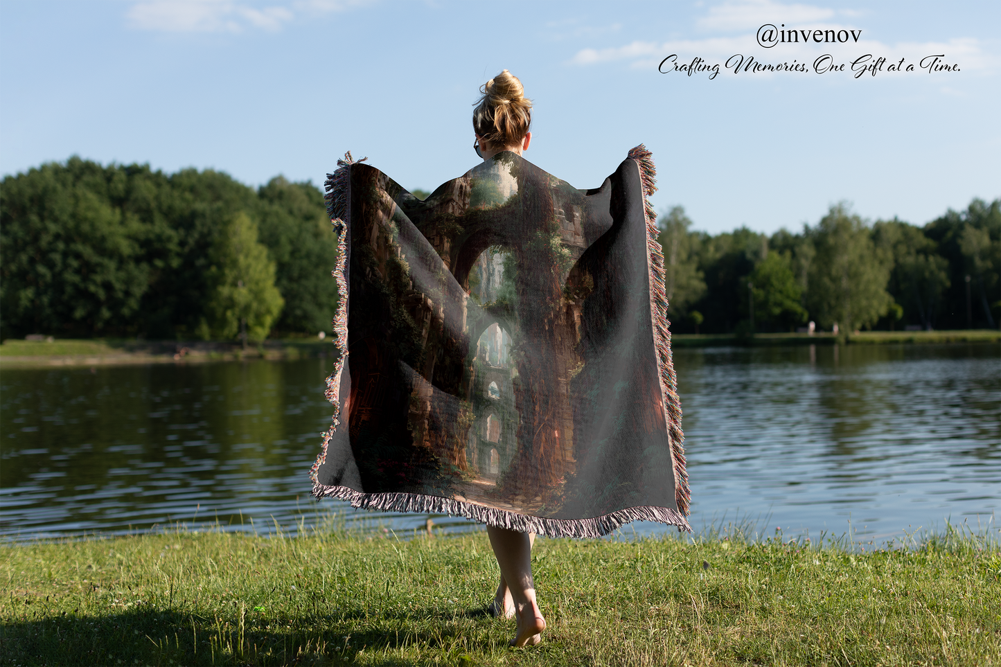 Person holding a large, patterned blanket by a lake with trees in the background