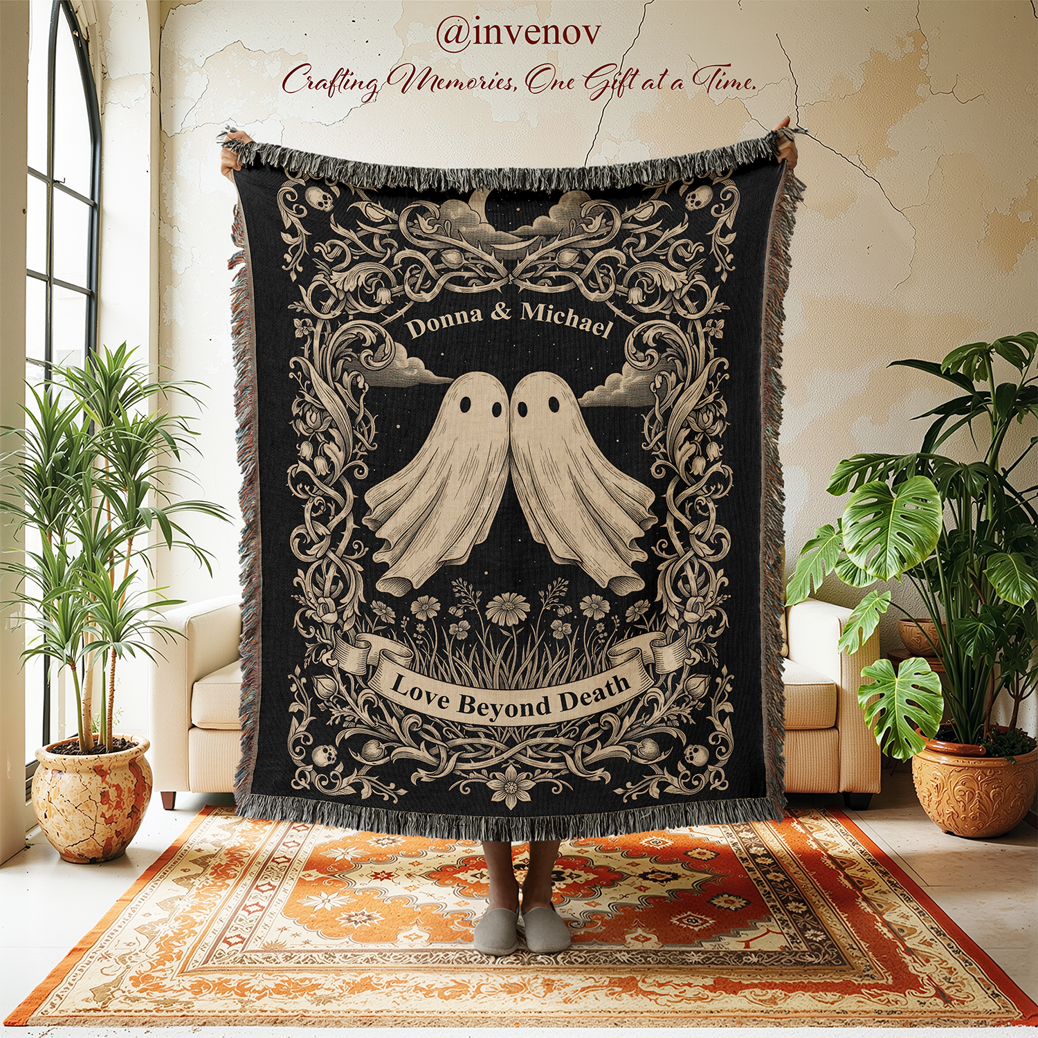 A person holds up a large black woven blanket or tapestry with fringe, featuring two cream ghosts, ornate scrollwork. The scene is set in a bright room with plants, a chair, and a patterned rug.