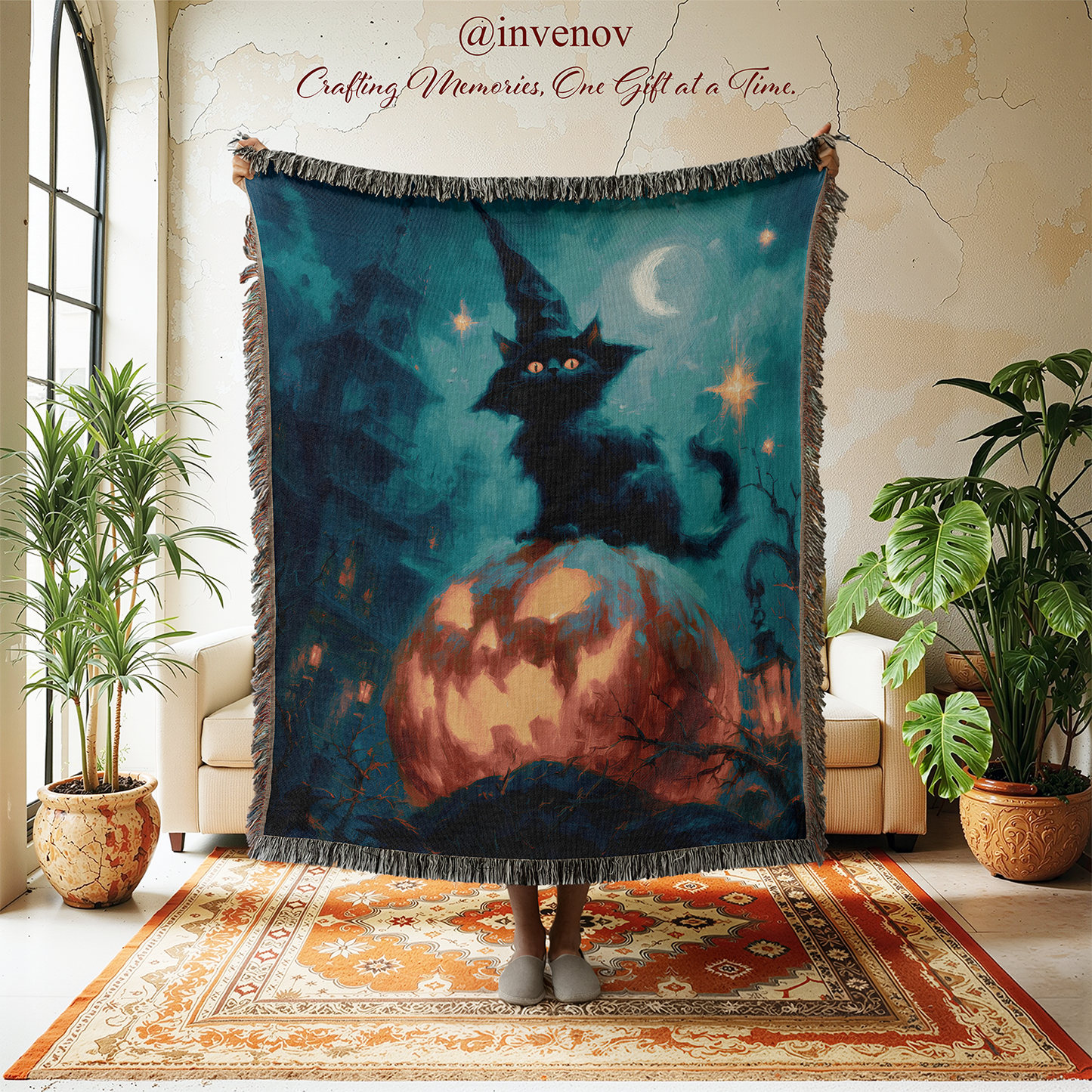A large woven throw blanket with fringe is held up in a room, featuring a dark witch cat sitting on a glowing orange moon under a crescent moon. The blanket is displayed in a cozy room setting with plants, a patterned rug, and a chair