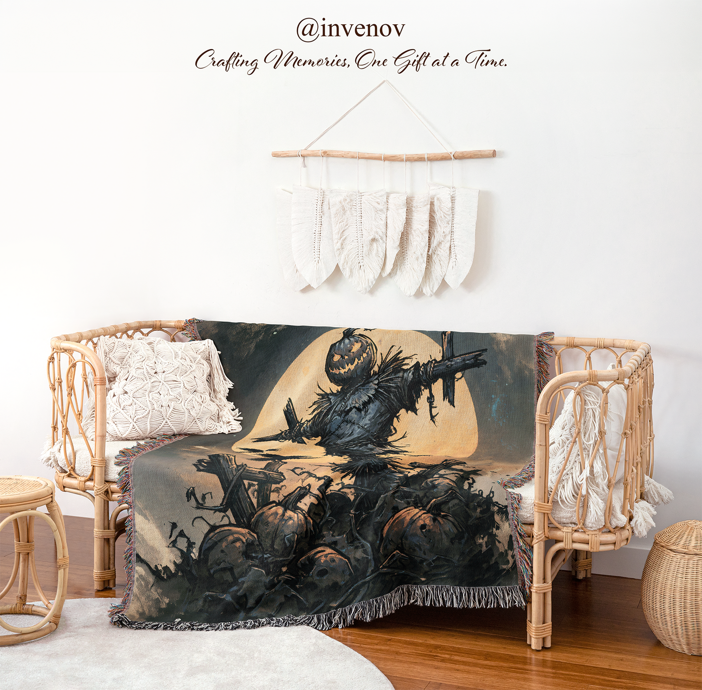 A Halloween-themed throw blanket draped over a rattan daybed in a styled room. The blanket features a dark illustration of a scarecrow, pumpkins, bats, and a large pale moon.