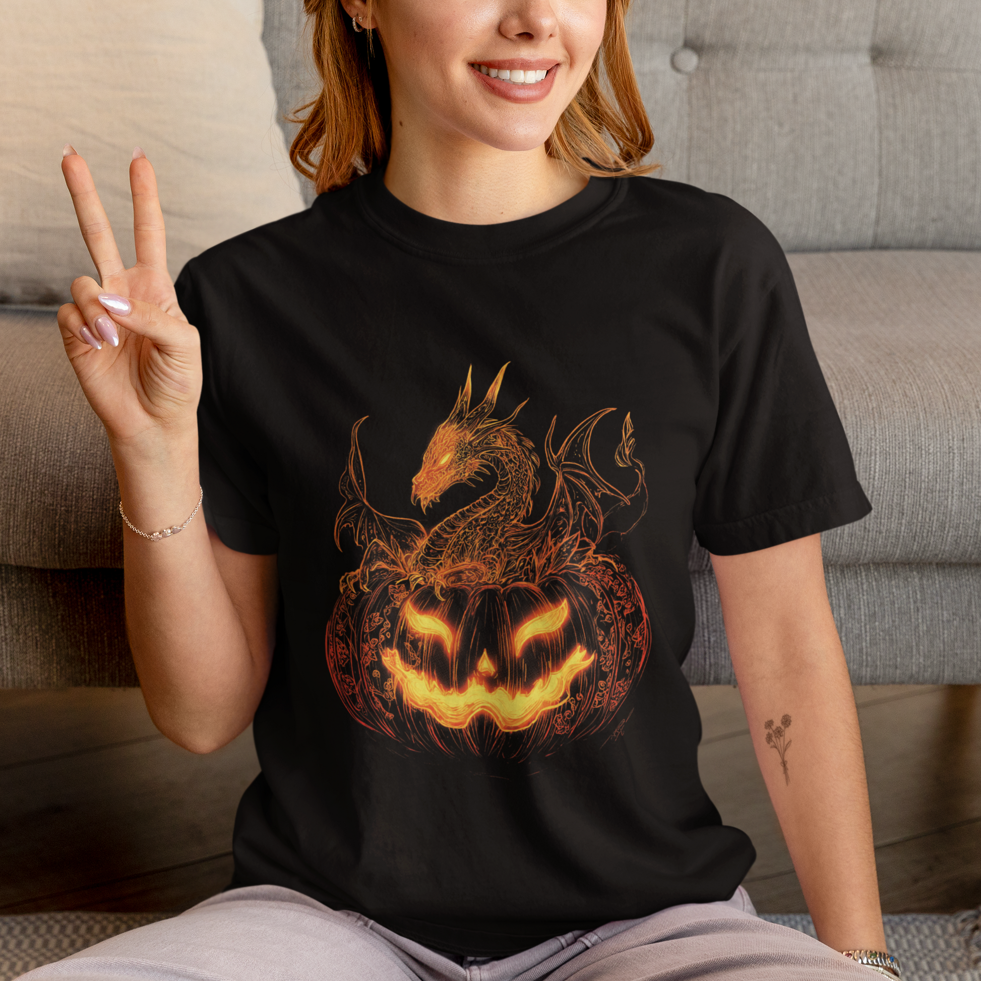 Person wearing a black t-shirt with a dragon and pumpkin design, sitting on the floor.
