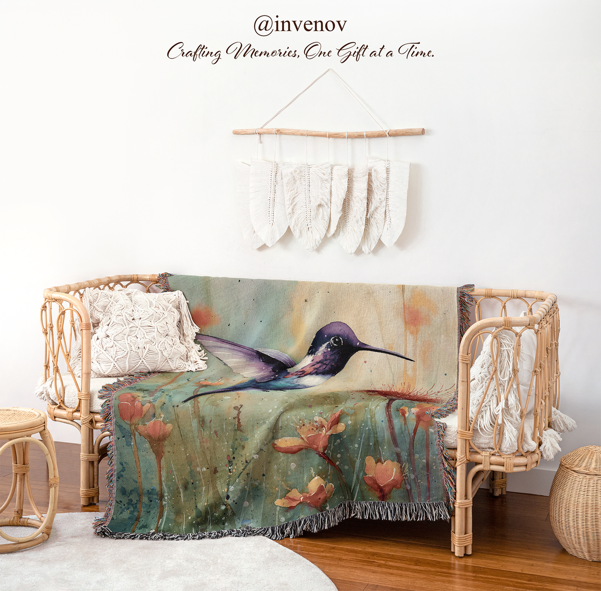 A woven rattan daybed in a styled nursery setting, draped with a colorful throw blanket featuring a hummingbird and water lilies. The room has a white wall with a macrame hanger, and the brand name '@invenov' is visible at the top.