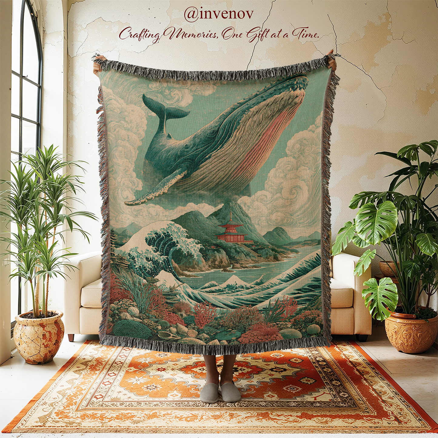 A large woven tapestry with fringe edges is held up in a styled room. The tapestry features a vintage-style illustration of a whale flying over waves and mountains, with a pagoda and clouds.