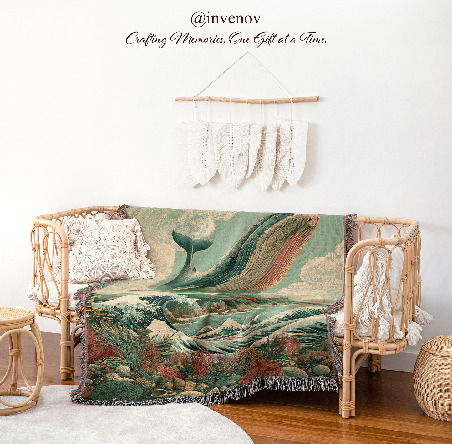 A woven throw blanket with a detailed whale and ocean landscape print is draped over a rattan daybed in a styled room setting. The scene includes a macrame wall hanging, wooden floor, and decorative pillows.