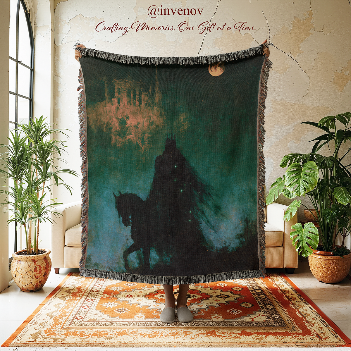 A large fringed throw blanket is held up in a styled room. The blanket features a dark teal and black fantasy-style print of a robed figure riding a horse, with a castle silhouette in the background and a small moon near the top right.