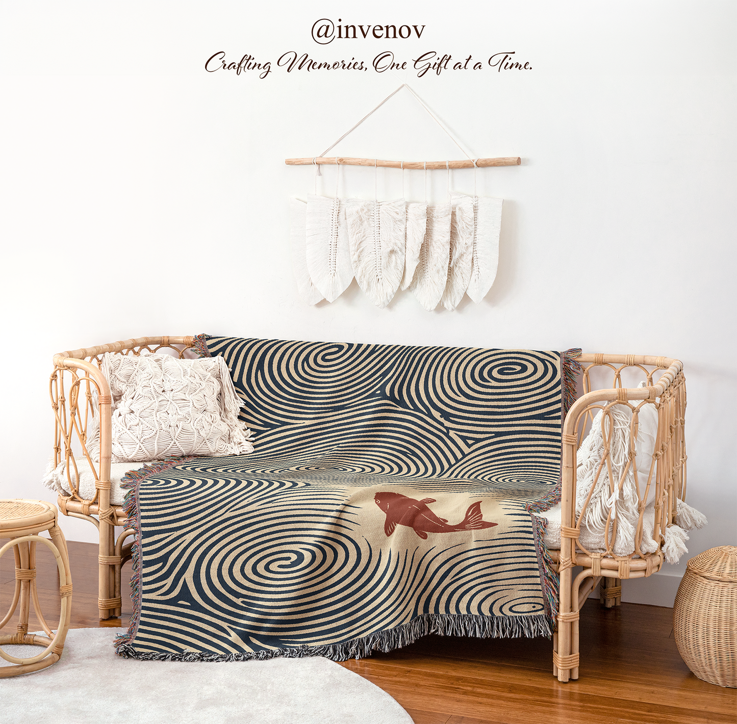 A woven throw blanket with a black and beige spiral pattern and a central red whale design, draped over a rattan daybed in a styled room setting.