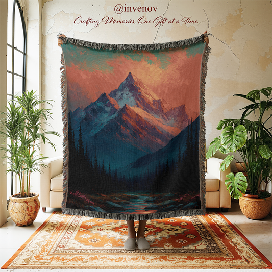 A large woven throw blanket with dark gray fringe is held up in a living room setting. The blanket features a scenic mountain landscape print with blue, teal, and orange tones.