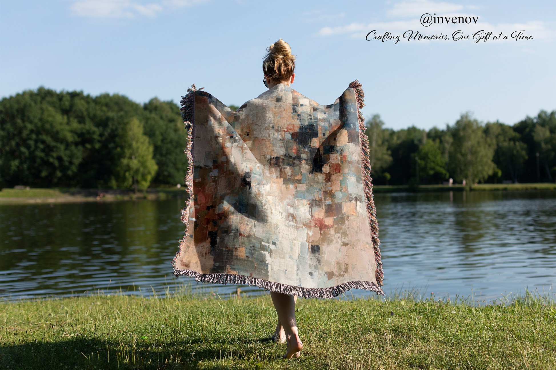 Person holding a colorful woven blanket by a lake with trees in the background