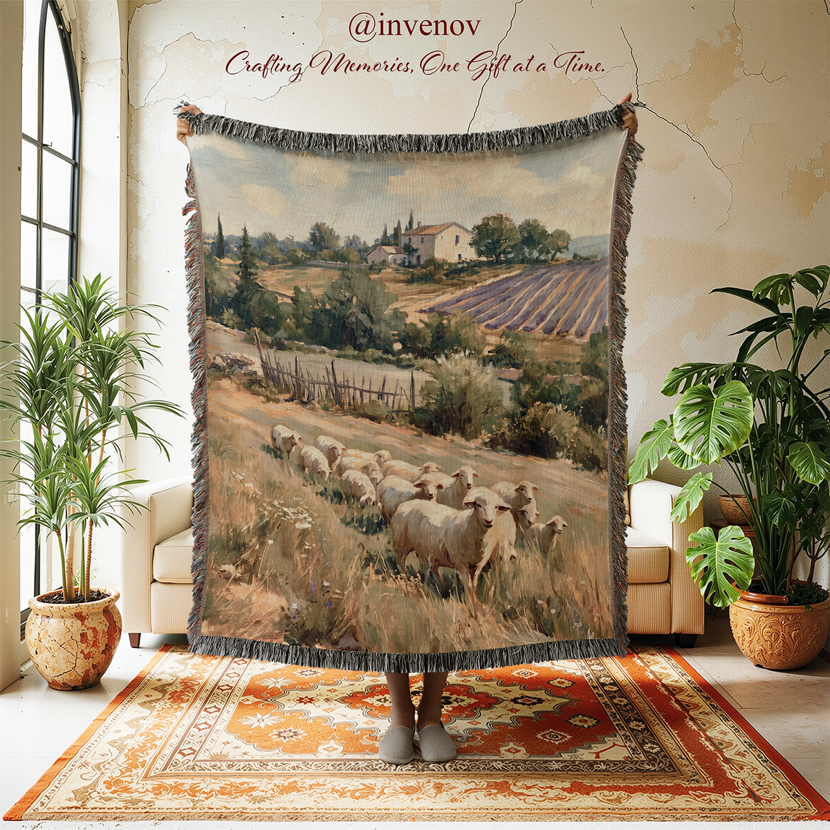 A large woven tapestry or throw blanket with fringe is held up in a bright room. The tapestry features a scenic landscape print of sheep grazing in a Tuscan field with a vineyard and a white house in the background.
