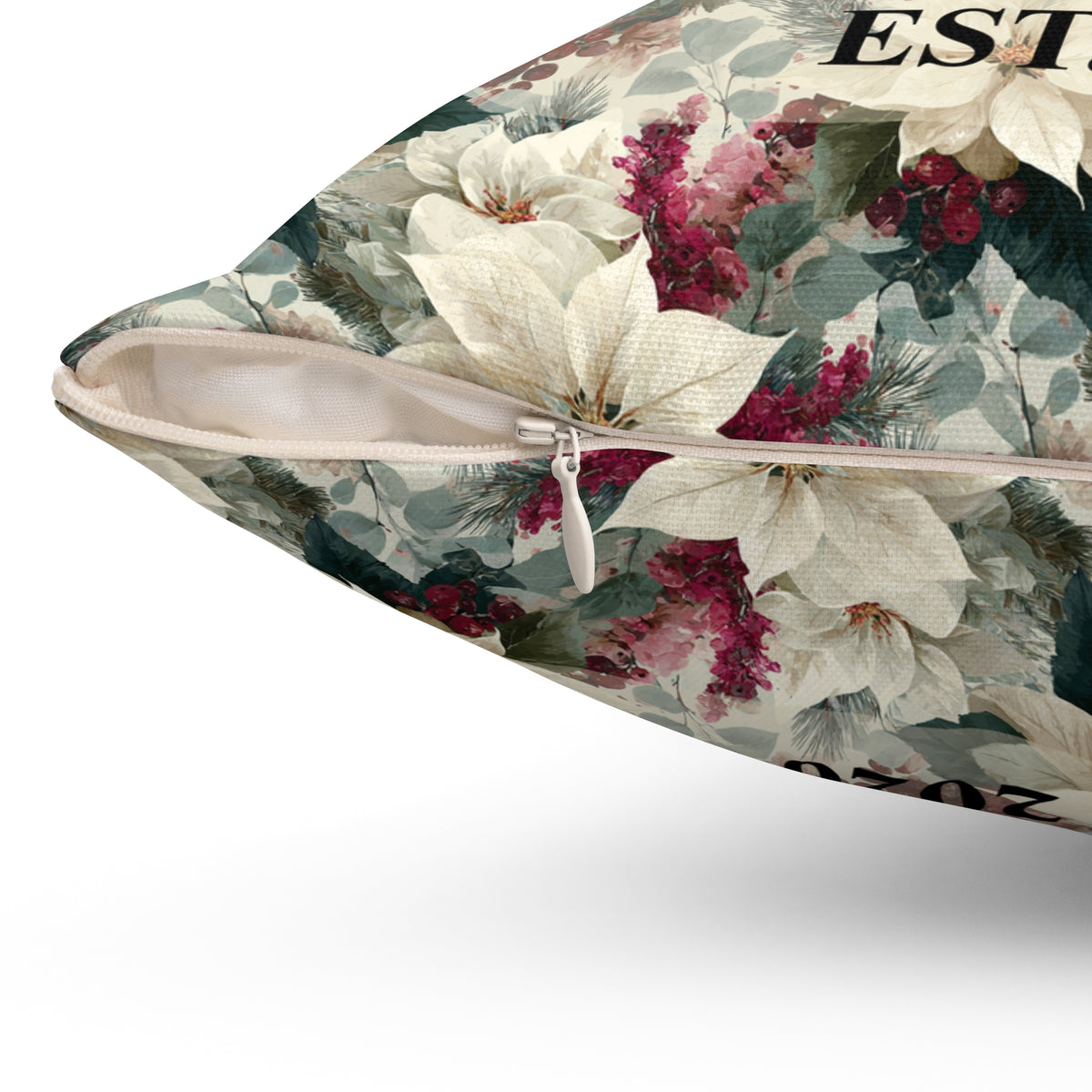 A close-up of a decorative throw pillow showing its floral print and zipper closure. The pillow features a pattern of white lilies, pink poinsettias, and green foliage on a light beige background.