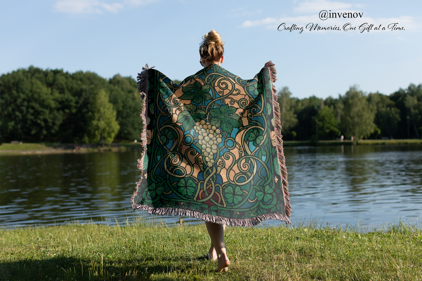 Person holding a decorative shawl by a lake with trees in the background