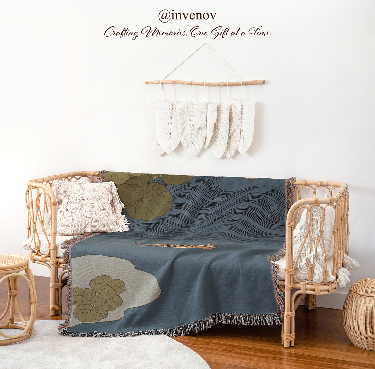 A navy blue throw blanket with a wavy line pattern and olive green leaf motifs is draped over a rattan daybed in a styled room setting