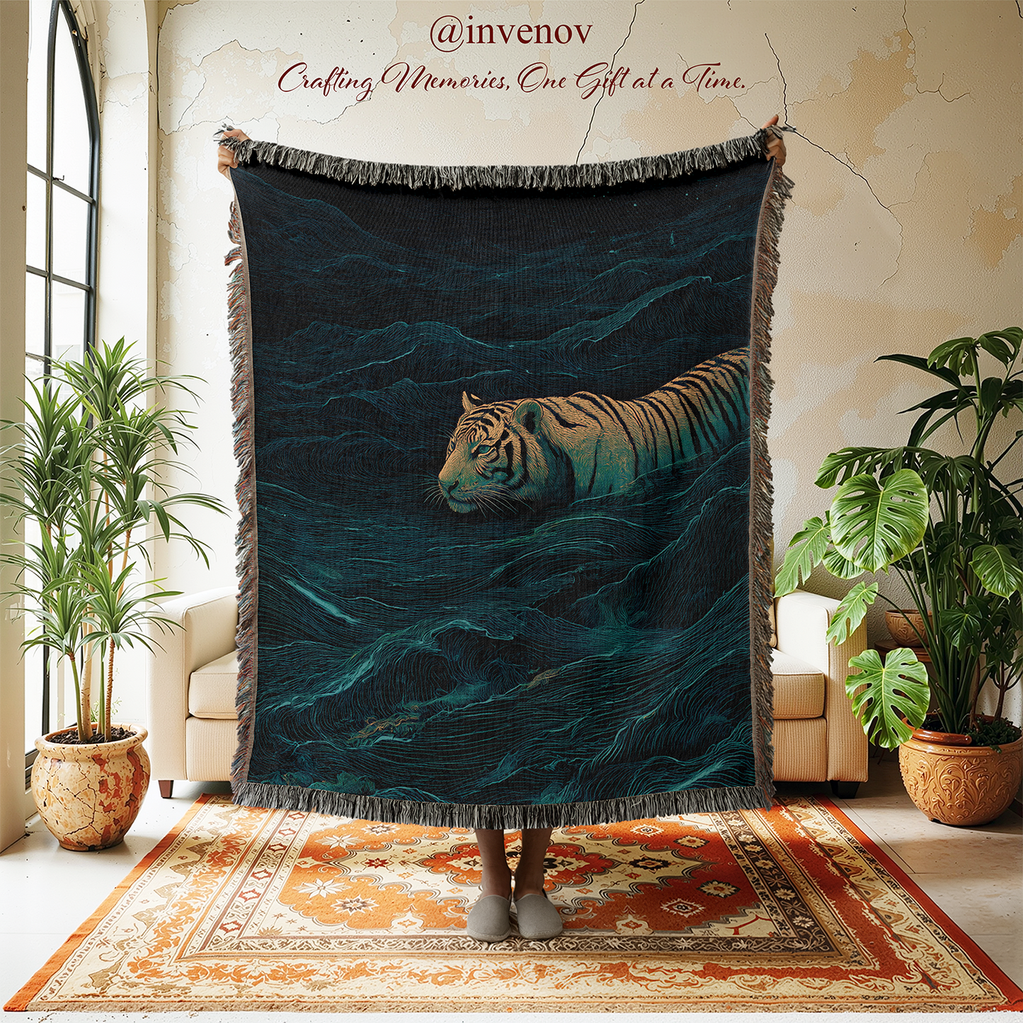 A person holds up a large fringed throw blanket in a styled room with plants, chairs, and a patterned rug. The blanket features an artistic print of a tiger swimming in dark teal and black water.