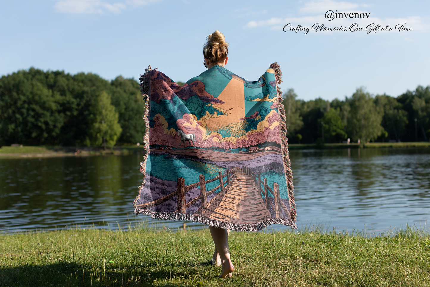 Person holding a colorful blanket with a scenic design by a lake