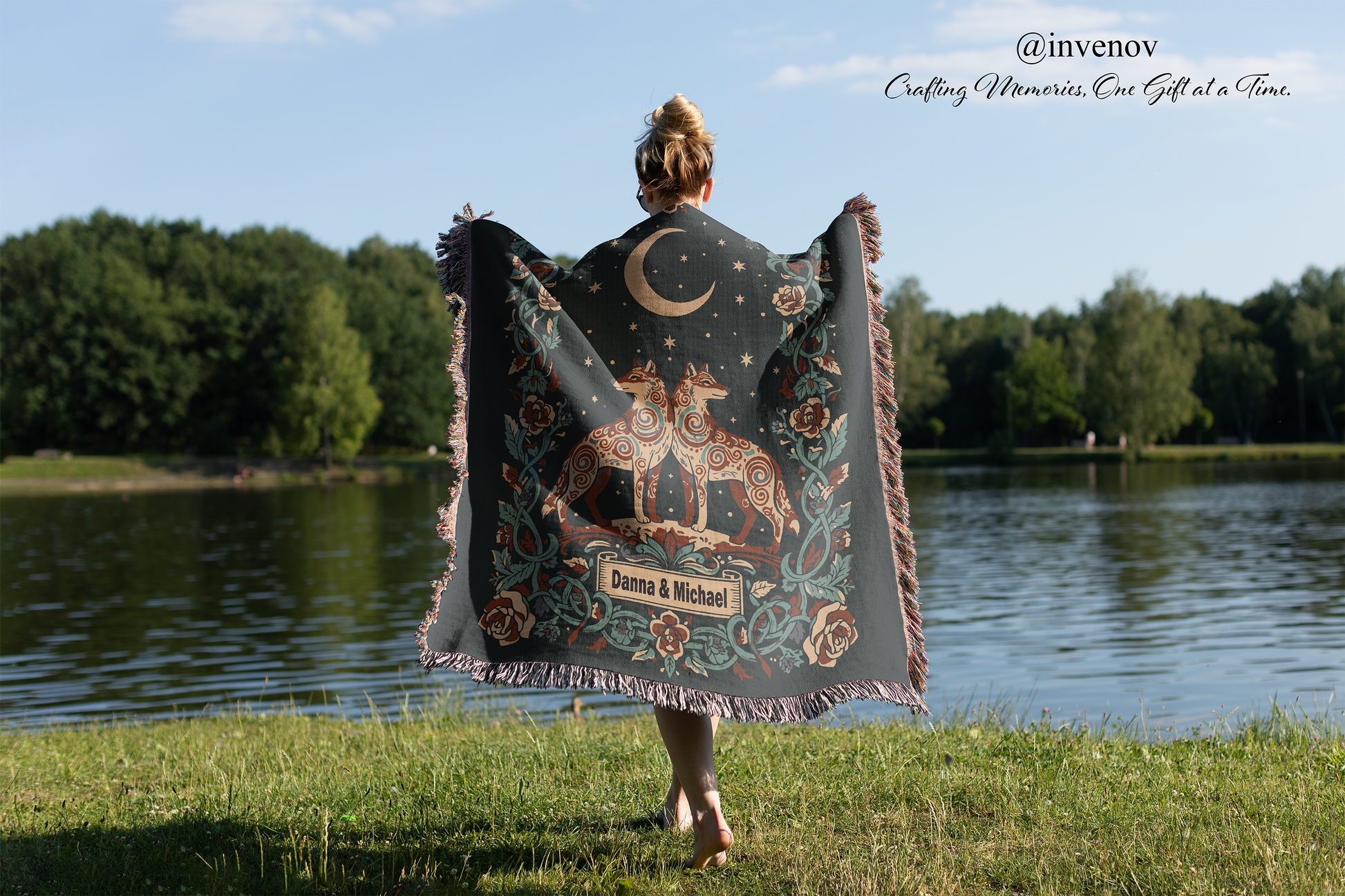 Person holding a decorative blanket with a nature-themed design by a lake.