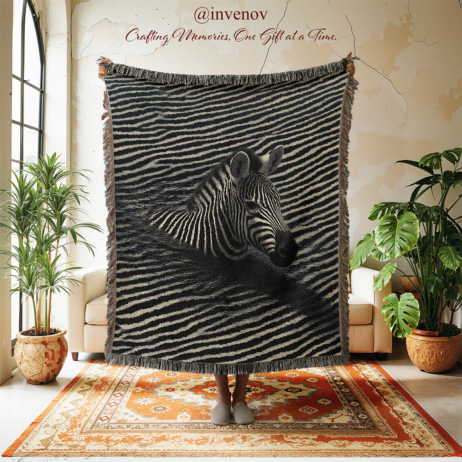 A large woven throw blanket with fringe is held up in a bright room. The blanket features a black and white zebra design on a dark background.